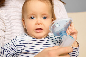 A caregiver holds a young child while they use a nebulizer for breathing treatment at home. The...