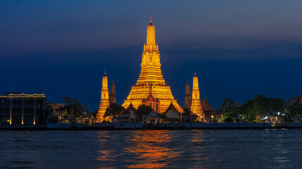 Wat Arun Ratchawararam Ratchawaramahawihan at sunset time Night lights.The foreground is the Chao Phraya River. It is a recommended tourist attraction in Bangkok, Thailand.