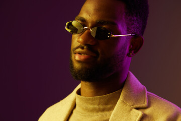 Obraz premium Stylish man wearing sunglasses and a beige coat against a purple background, exuding confidence and modern fashion trends