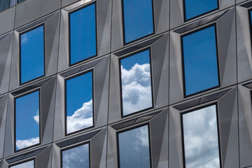 An artistic view of a modern building facade featuring reflective glass windows, capturing the blue sky and clouds, creating a harmonious connection between nature and architecture.