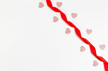 Top view of red ribbon and pink glitter hearts on white background. Valentine's day, love. Shiny rolled fabric, silk and satin material. Copy space, flat lay.