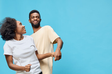 Obraz premium A joyful young couple dancing together against a vibrant blue background, showcasing happiness, connection, and fun in casual attire