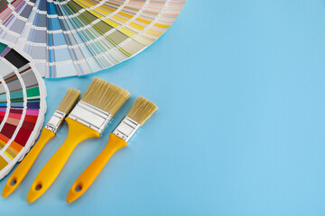 Color selection charts and paint brushes on light blue table, space for text. Decorating and design