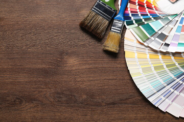 Color selection charts and paint brushes on wooden table, flat lay with space for text. Decorating and design