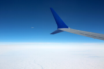 Aerial view from airplane window with airplane wing and plane far away.