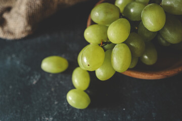 Fresh green grapes in a wooden bowl with rustic background, placed on a dark textured surface. Healthy and organic fruit concept