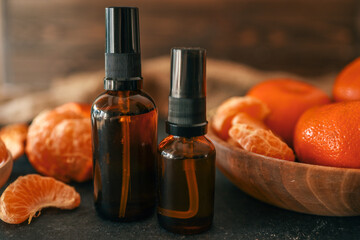 Two amber spray bottles on a dark surface, surrounded by fresh mandarin slices and whole fruits....