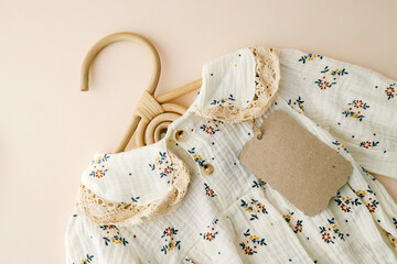 Close-up of a floral baby dress with lace details and an eco-friendly kraft paper tag on a soft...