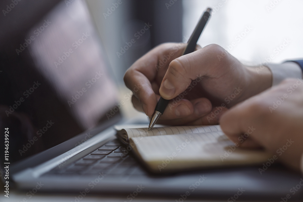 Poster a man's hand inscribing in a notepad on a modern laptop, captured closely, with a vague background