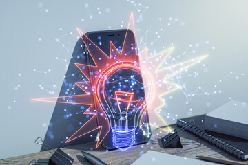 Abstract holographic light bulb glowing over a smartphone on a desk.