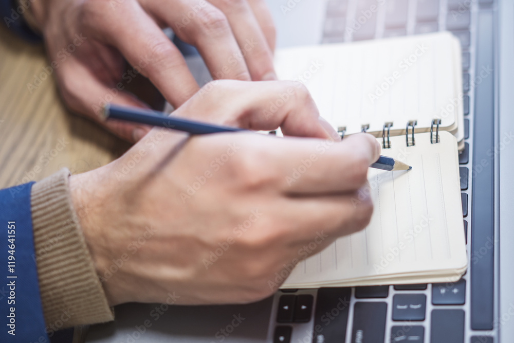 Poster a man's hand is caught in close-up, busily writing in a notepad on a laptop, while the background is