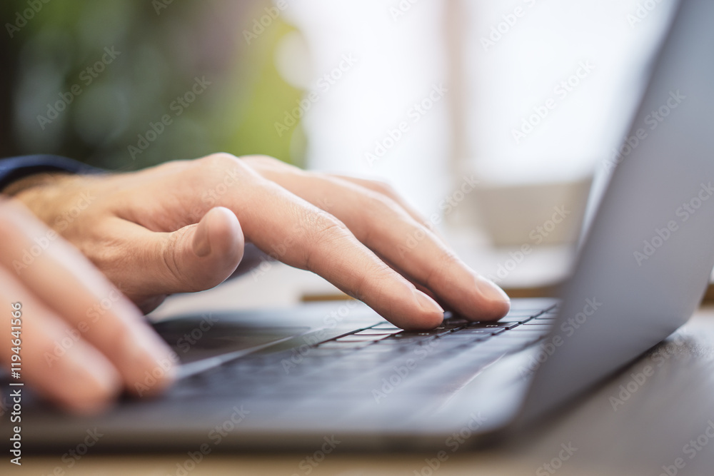 Poster against a blurry office backdrop, a close-up view reveals a man's hands as they type on a sleek lapt