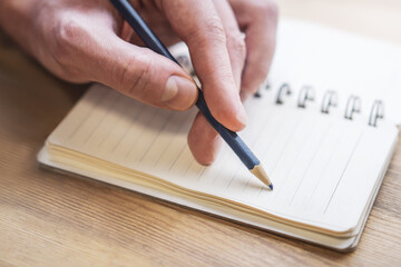 Sharp view of a man's hand transcribing in a notepad, with a defocused backdrop