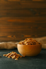 A wooden bowl filled with crunchy breakfast cereal flakes on a dark surface with rustic fabric in the background. Perfect for illustrating breakfast or healthy eating concepts