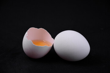 One whole and one broken egg on a black background. The minimalistic and aesthetic design is suitable for advertising cooking, healthy eating and farm products.