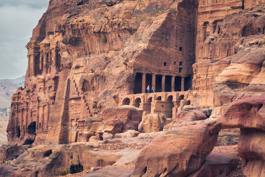 The view of Nabatean Kings Royal Tombs surrounded by high sandstone cliffs during a day time, in a scale with a human, Unesco world heritage site, Petra, Jordan, Middle East