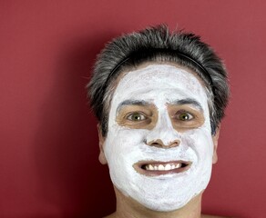 Fototapeta premium A handsome mature Caucasian man in his fifties with green eyes and gray hair cares for his complexion with a white clay face mask