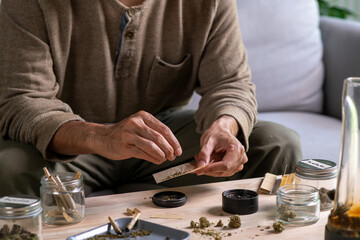 Asian man carefully rolling a cannabis joint in a cozy living oom, surrounded by a relaxed ambiance...
