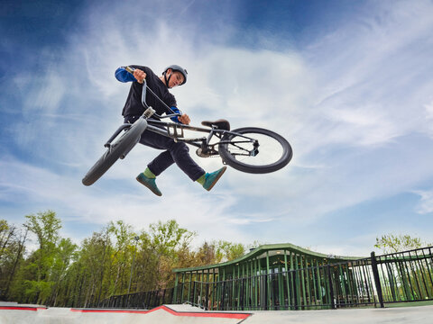 BMX bicycle rider doing stunt Tailwhip in quarter pipe. Skilled BMX freestyler athlete jumping over quarter ramp and doing aerial trick Tailwhip in street ramp park outdoors - Powered by Adobe