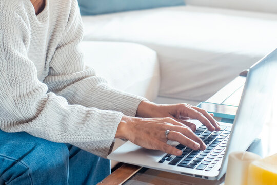 A mature woman working from home, sitting on a couch with a laptop, browsing social media, managing her online business, chatting, and enjoying her time in a casual and productive home office setup