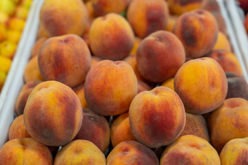 A pile of peaches with a few apples in the background. The peaches are ripe and ready to eat
