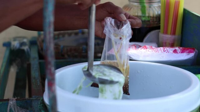 Close up A 'Dawet' ice seller is placing the dawet ice ordered by the buyer in plastic bag, Indonesian Iced Sweet Coconut Drink" or "Iced Dawet