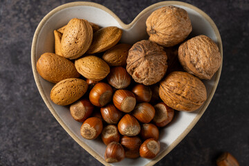 Mix of nuts in a heart shaped bowl, hazelnuts, almonds, walnuts, top view