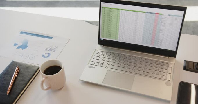 Working from home, laptop displaying spreadsheet next to coffee cup and documents