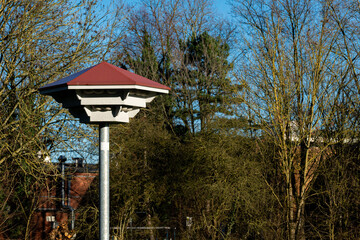 A distinctive structure with a red roof stands tall amidst lush green trees under a clear blue sky. The contrast of design and nature creates an eye-catching view.