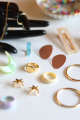 Hand figurine, sunglasses, gold jewelry, colorful bead jewelry, statement rings and various hair accessories on the white table. Selective focus.