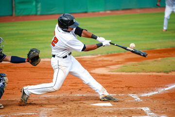 Baseball player makes contact with the ball, executing a powerful swing during a daytime game.