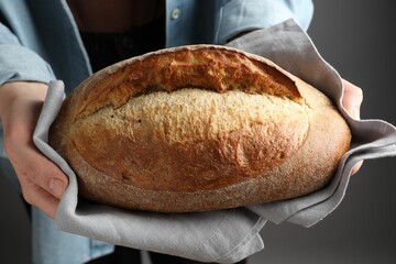 Woman with loaf of freshly baked bread on grey background, closeup