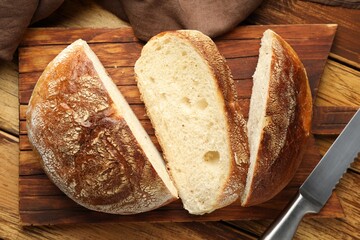 Cut loaf of fresh bread and knife on wooden table, top view