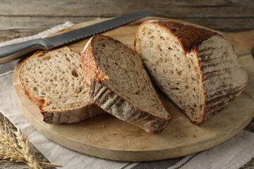Cut loaf of fresh bread and knife on wooden table, closeup