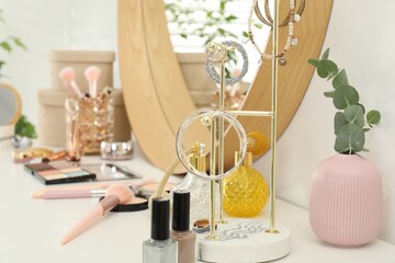 Makeup room. Mirror, jewelry and different cosmetic products on white dressing table indoors, closeup