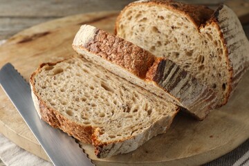 Cut loaf of fresh bread and knife on table, closeup