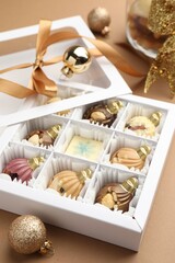 Delicious chocolate in shape of ornaments in open box and Christmas decor on beige background, closeup