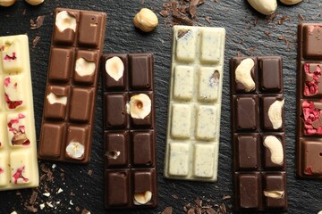 Different tasty chocolate bars with nuts and freeze dried raspberry on black table, flat lay