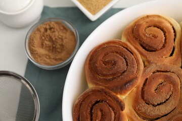 Tasty cinnamon rolls and spices on white table, flat lay