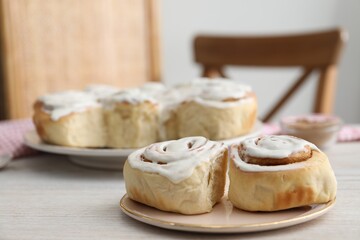 Delicious frosted cinnamon rolls on light wooden table indoors, closeup