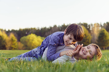 Fototapeta premium Positive emotions. Two happy laughing teenage boys, friends, brothers are lying on grass of lawn.