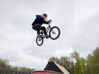 BMX bicycle rider doing stunt jump over spinу in quarter pipe. Skilled BMX freestyler athlete jumping over quarter ramp and doing aerial trick Tailwhip in street ramp park outdoors