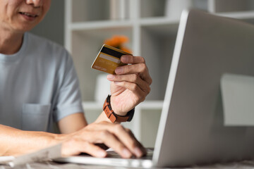 Close-up of a senior man with a credit card shopping online at home using a laptop