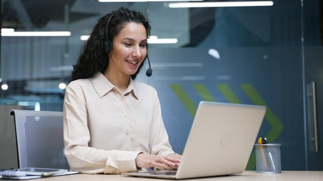 Female corporate operator in headset working in customer support service on helpline telesale talking using laptop sitting in business office. Agent of call center advises client, answering questions