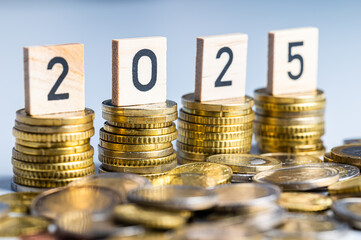 Piles of coins, and wooden cubes that spell out the number 2025. New year, economy and wealth.
