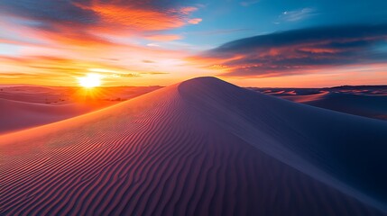 a sand dune with the sun setting behind it