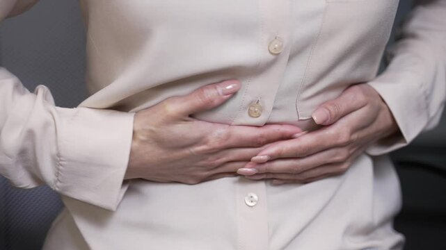 Close up. Female hands holding massaging stomach. Businesswoman feels stomach pain while sitting at workplace in business office. Sick woman suffers from gastritis, menstruation, poisoning or bloating