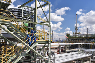 Workers in work clothes in a rafinery - modern equipment and buildings of the factory for production of fuel and gas from petroleum
