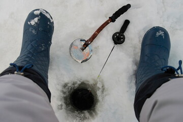 woman sitting by the hole with a fishing rod during winter fishing