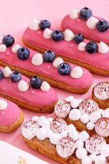 different types of eclairs decorated with cream and blueberries isolated on pink background